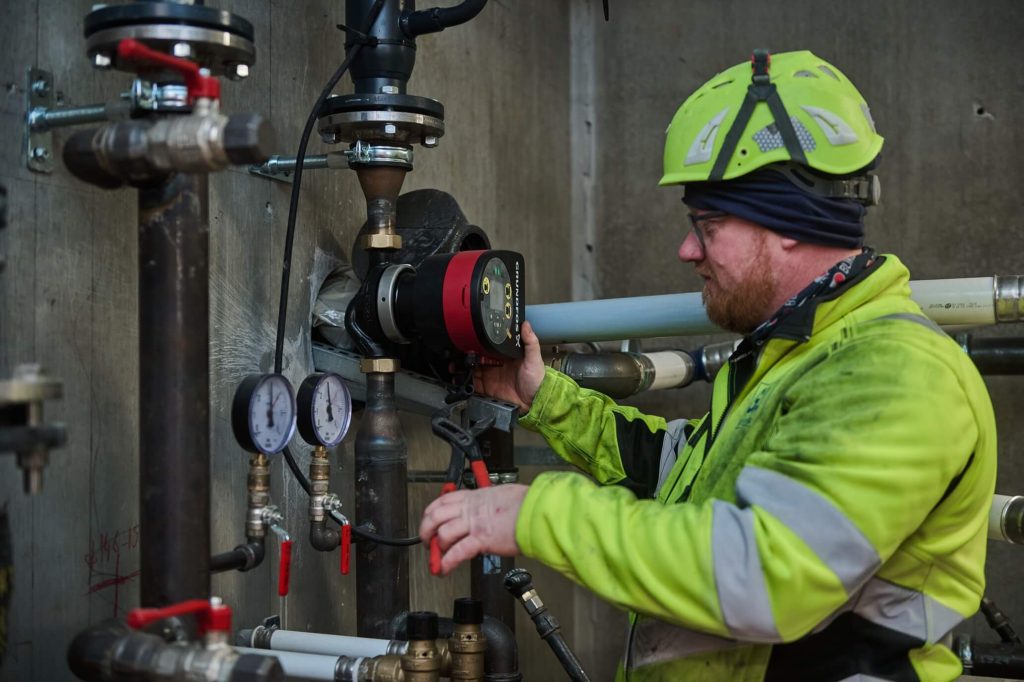 A man wearing a safety jacket and helmet is working on a pipe at a construction site.